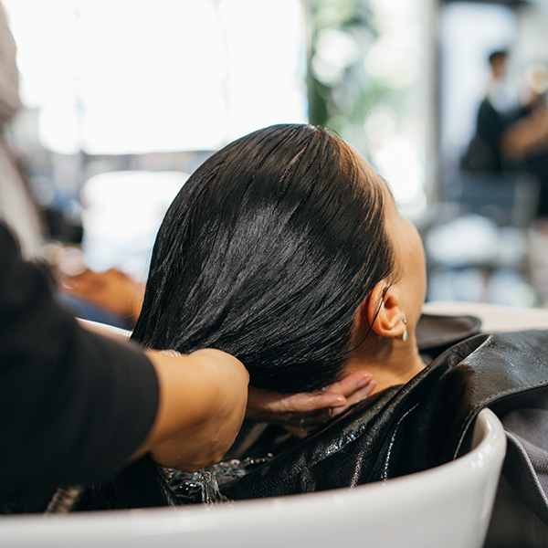 Young Caucasian woman at the hairdresser pampering herself by getting her hair washed and rinsed with eyes closed with head in sink for hairwash